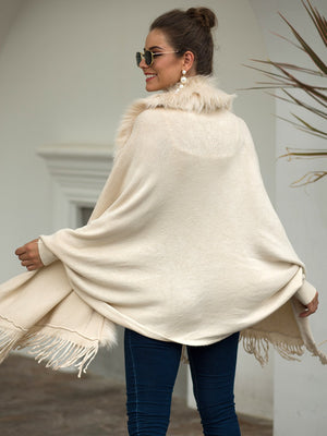Ivory knit cape with faux fur trim and fringe detailing.