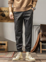 Men's dark gray slim fit ankle pants with cuffed hems, styled with a tan sweatshirt and boots.