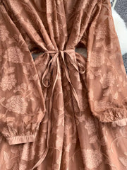Embroidered tie-waist dress in rust with sheer floral pattern and long sleeves.