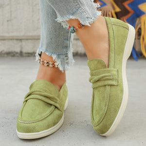 Green suede slip-on loafers with a decorative knot detail and white soles.