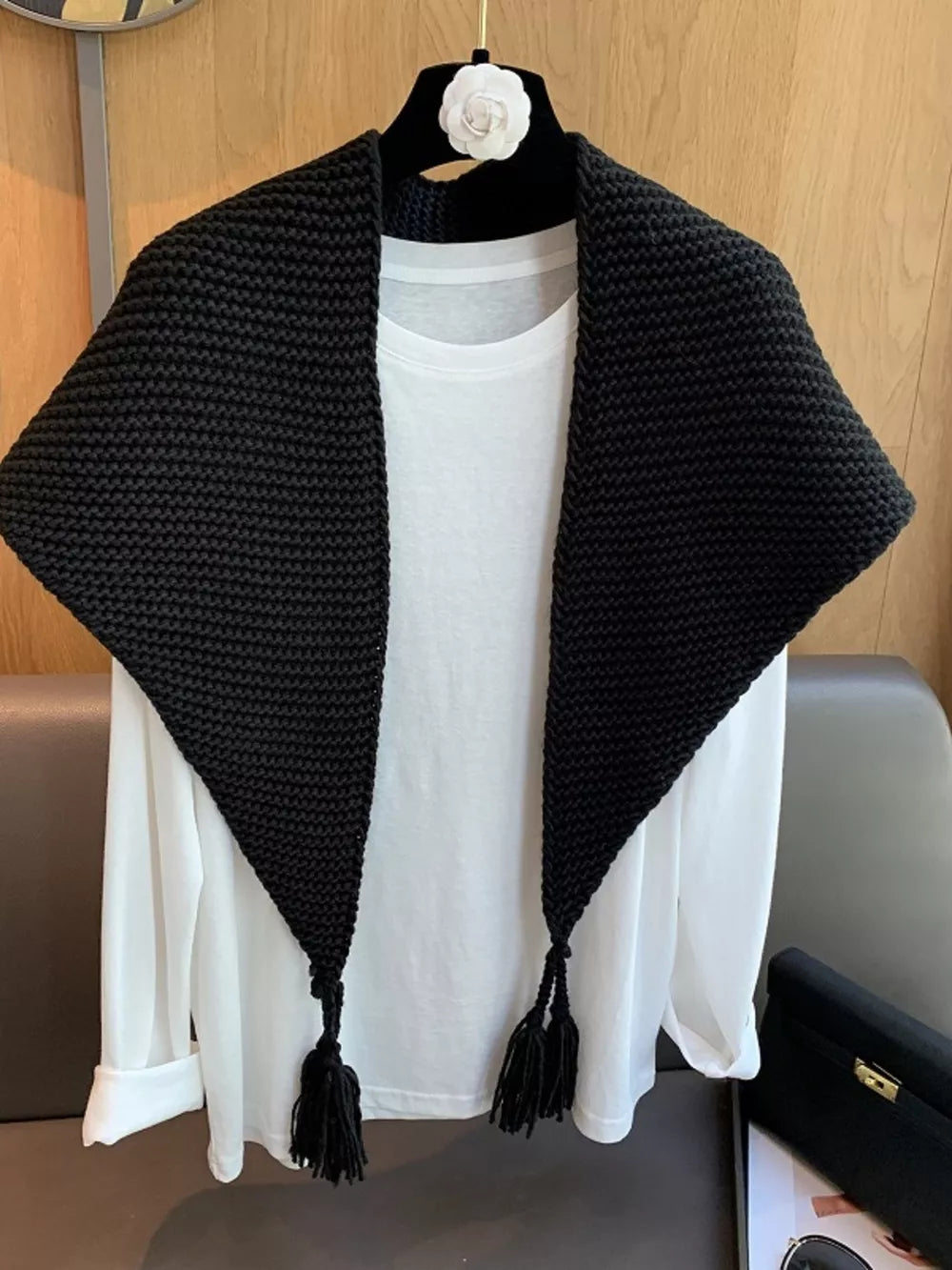 Black chunky knit scarf accessory with tassels, styled over a white shirt.