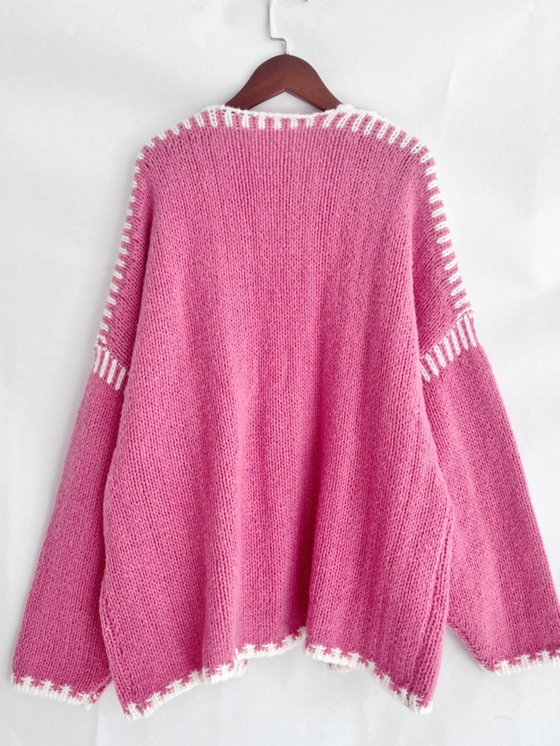 Pink oversized knit cardigan with contrast white stitching detail on neckline, cuffs, and hem.