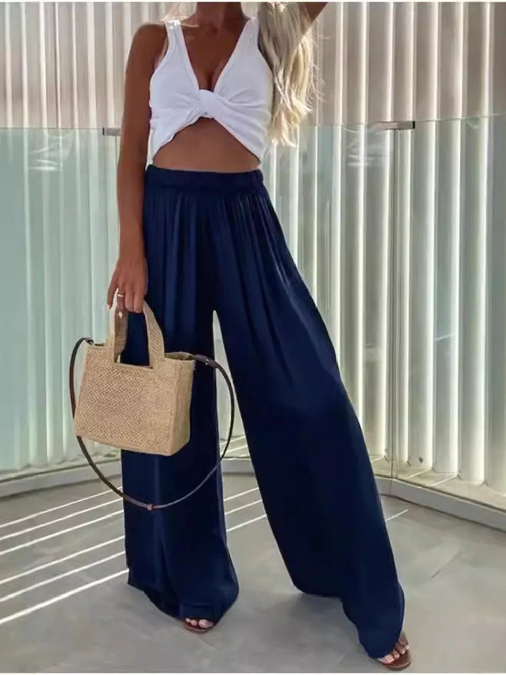 Dark blue maternity pants with paperbag waist and wide legs, styled with a white crop top and straw bag.