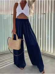 Dark blue maternity pants with paperbag waist and wide legs, styled with a white crop top and straw bag.