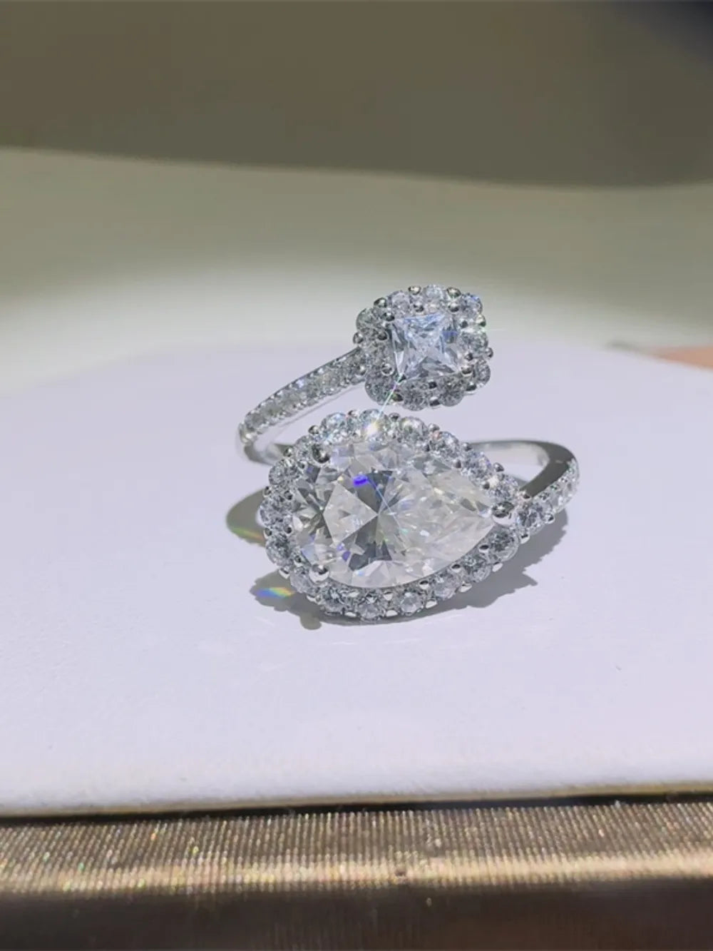 Silver bypass engagement ring with pear and square cut diamonds, halo setting.
