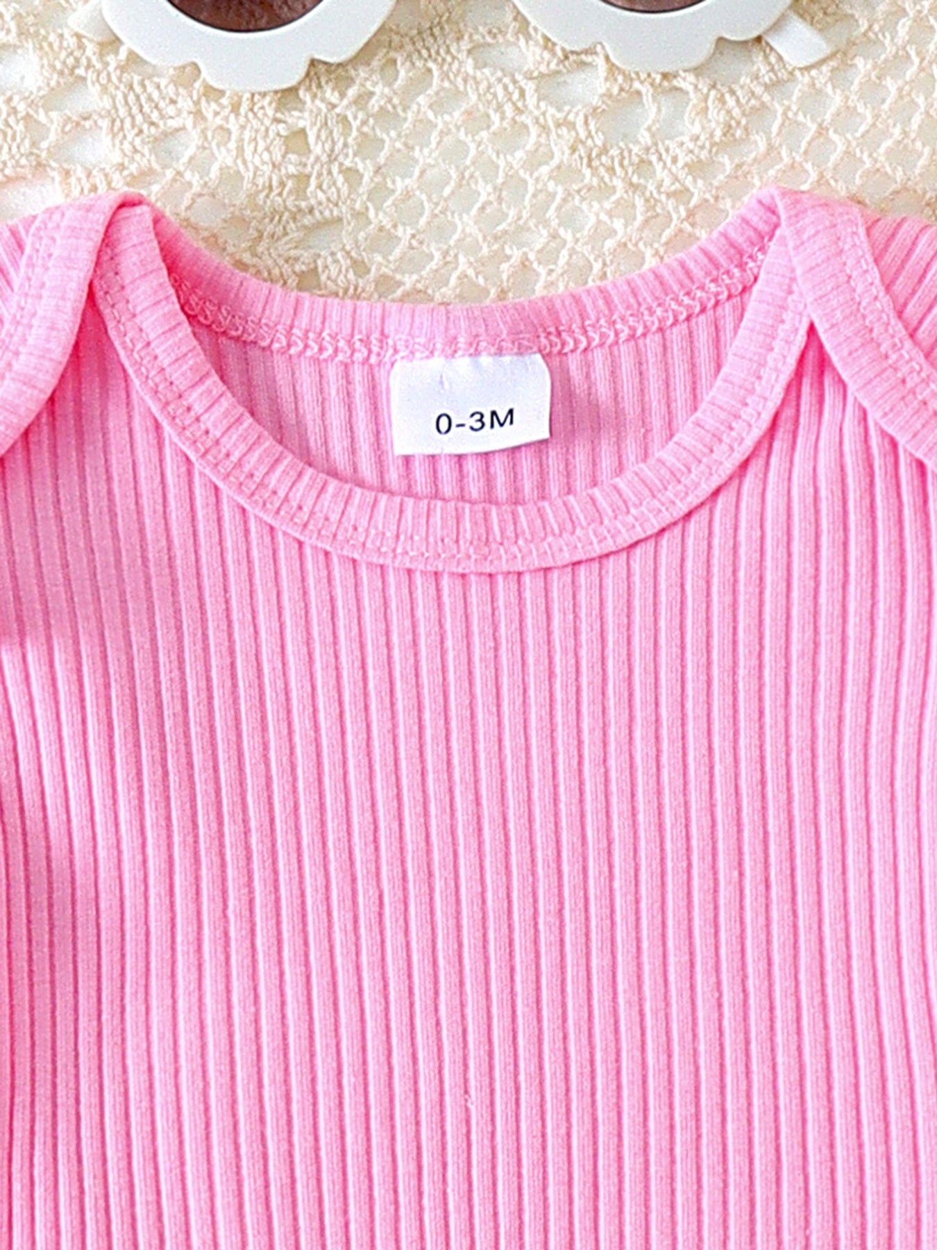 Pink ribbed cotton baby top with ruffle trim and daisy overalls detail