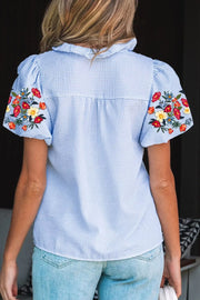 Blue striped cotton shirt with embroidered floral puff sleeves and ruffled collar.