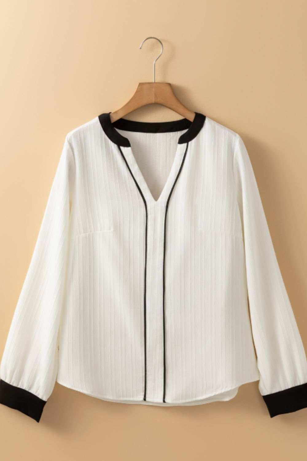 White textured V-neck blouse with black trim and cuffs.