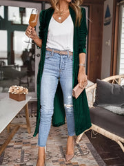 Dark green velvet duster coat with fluid silhouette, open front, long sleeves, worn with jeans.