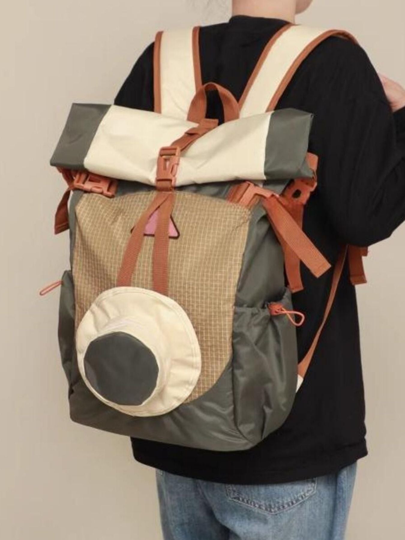 Sleek roll-top nylon backpack in moss green, cream, and tan with orange accents and a hat attachment.