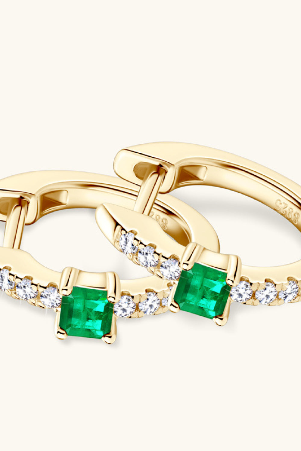 Gold huggie hoop earrings with emerald and pave diamond details.