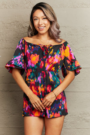 Off-shoulder playsuit with abstract print, tie detail, and ruffled sleeves.