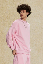 Oversized crewneck sweatshirt in blush pink with subtle shoulder detail and relaxed fit.