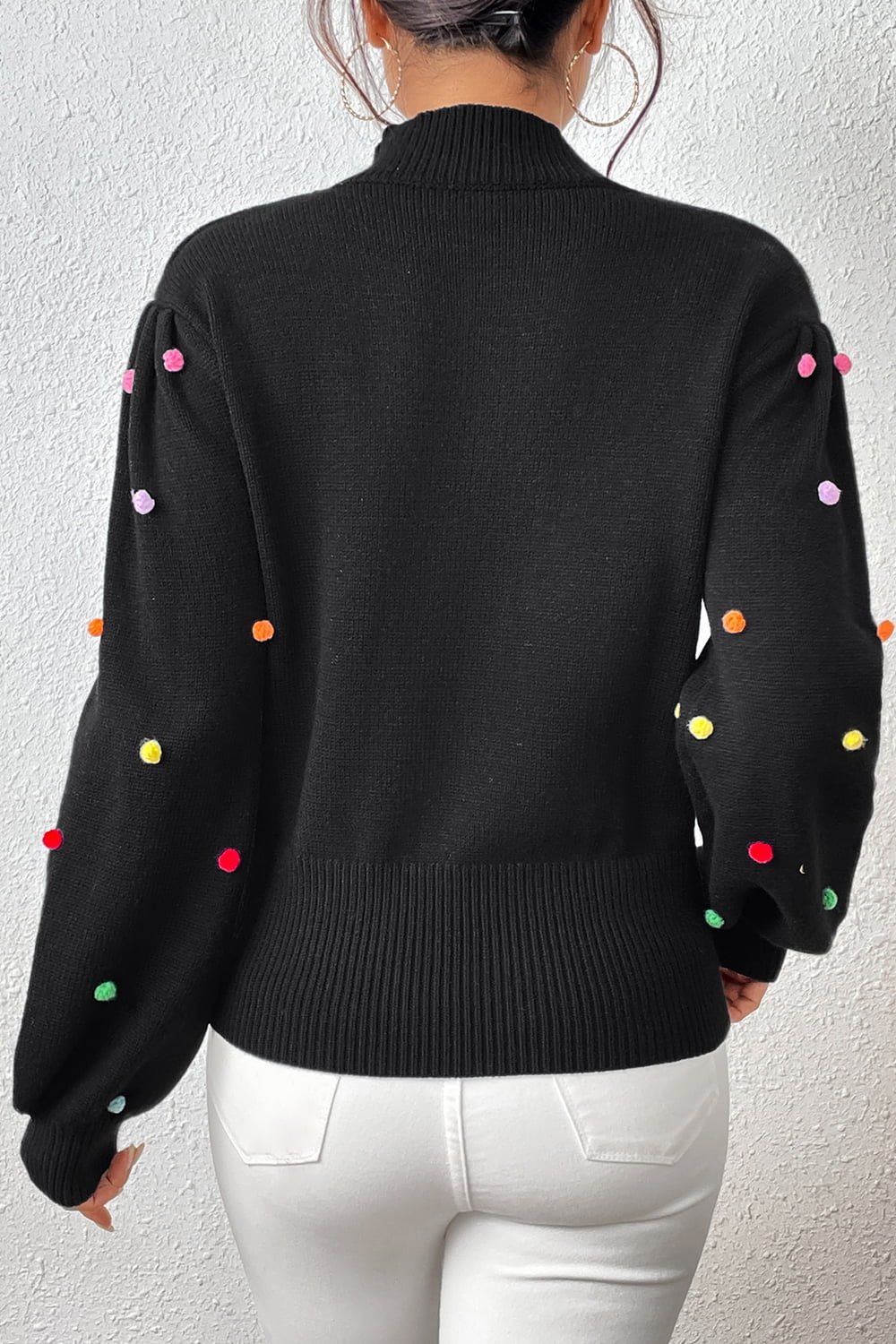 Black blouson sweater with colorful pom-pom embellishments on the sleeves.