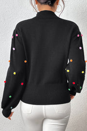 Black blouson sweater with colorful pom-pom embellishments on the sleeves.
