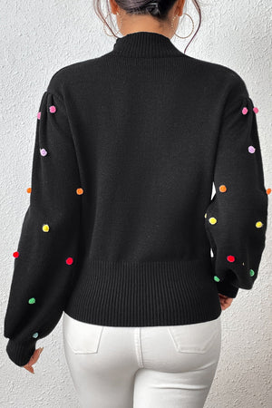 Black blouson sweater with colorful pom-pom embellishments on the sleeves.