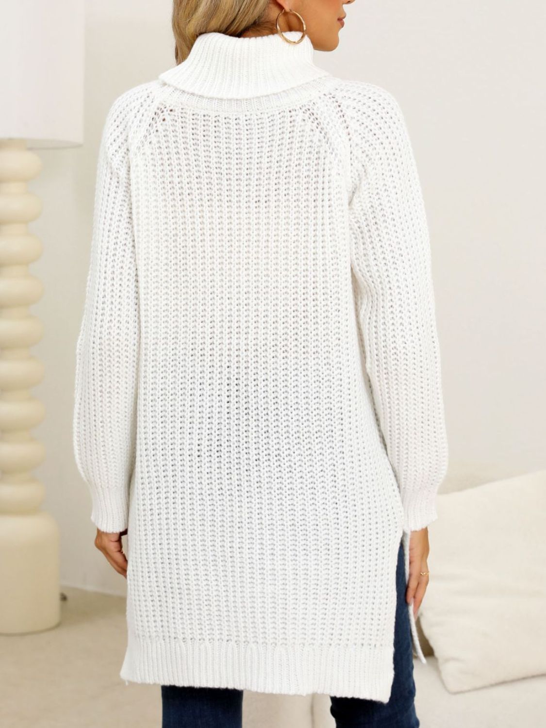 White knit turtleneck sweater with asymmetric hemline and ribbed texture.