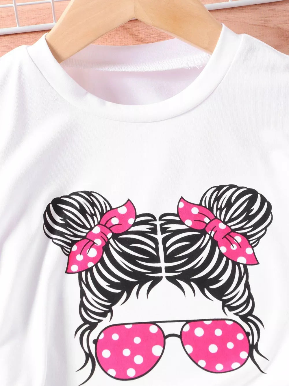 White graphic tee with cartoon girl and pink polka dot bows and sunglasses.