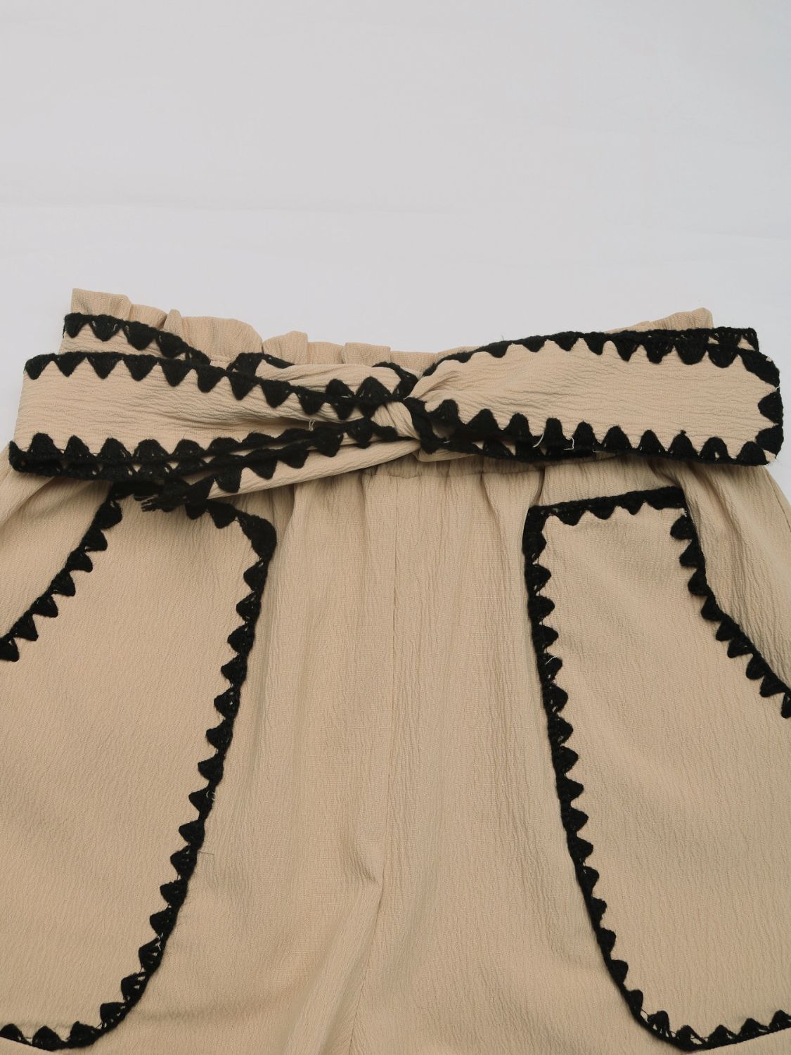 Tan paperbag shorts with scalloped black trim and a tie waist.
