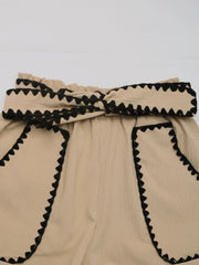 Tan paperbag shorts with scalloped black trim and a tie waist.