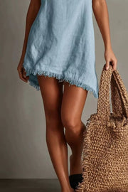 Light blue cotton cami dress with fringe trim and V-neck, styled with a straw bag.