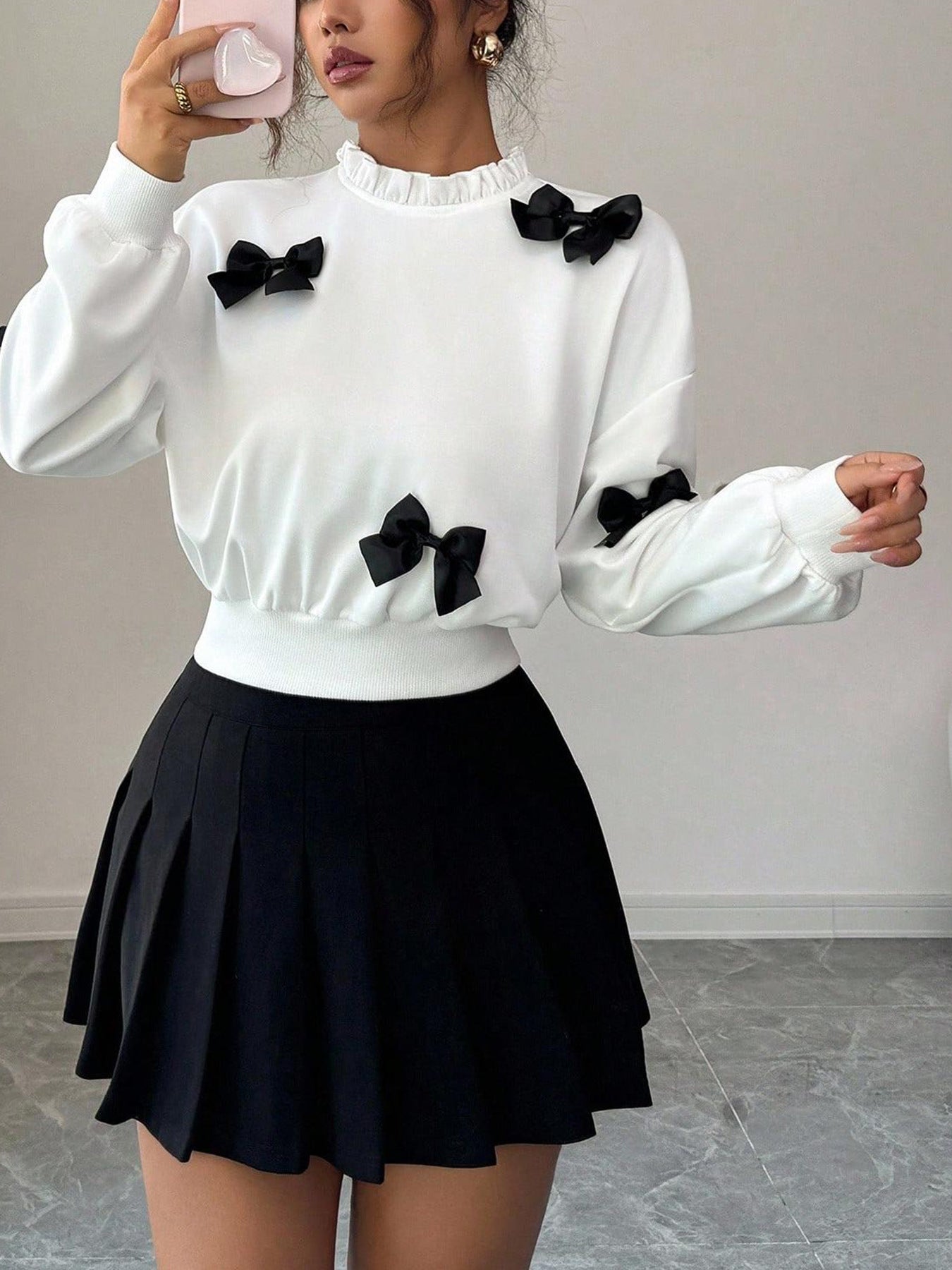 White crew neck sweatshirt with black bow appliques and ruffled neckline.