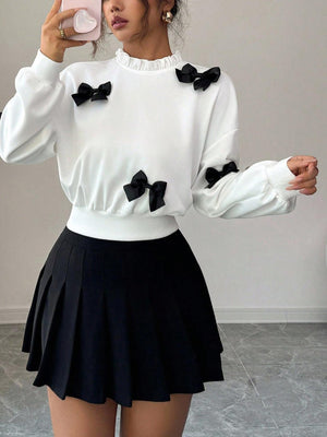 White crew neck sweatshirt with black bow appliques and ruffled neckline.
