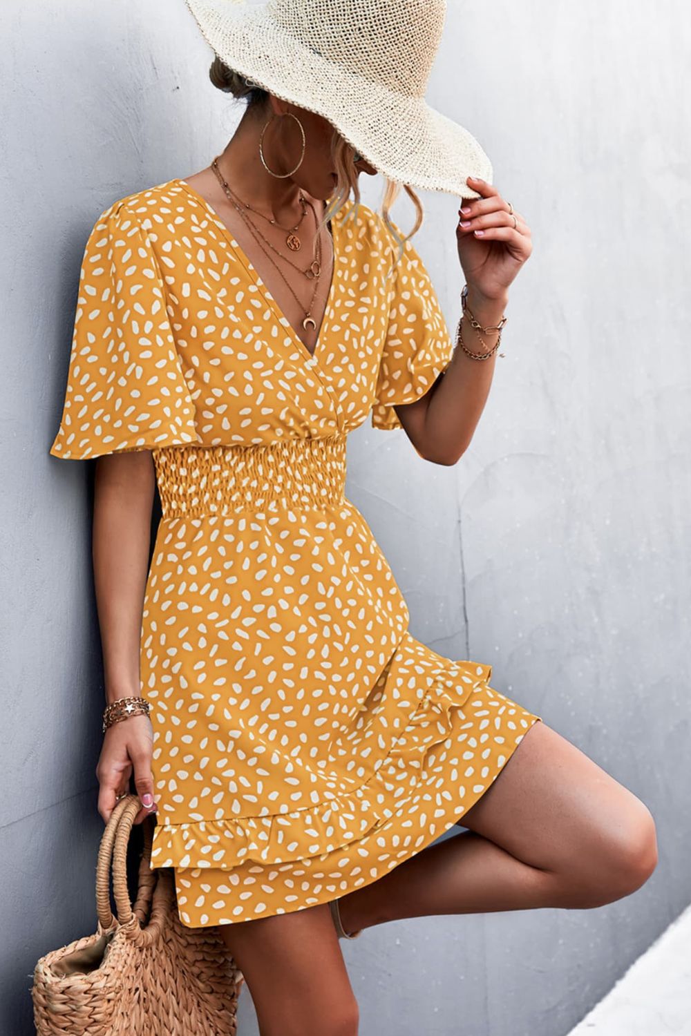 Mustard smocked waist mini dress with white speckle print, V-neck, flutter sleeves, and ruffled hem.