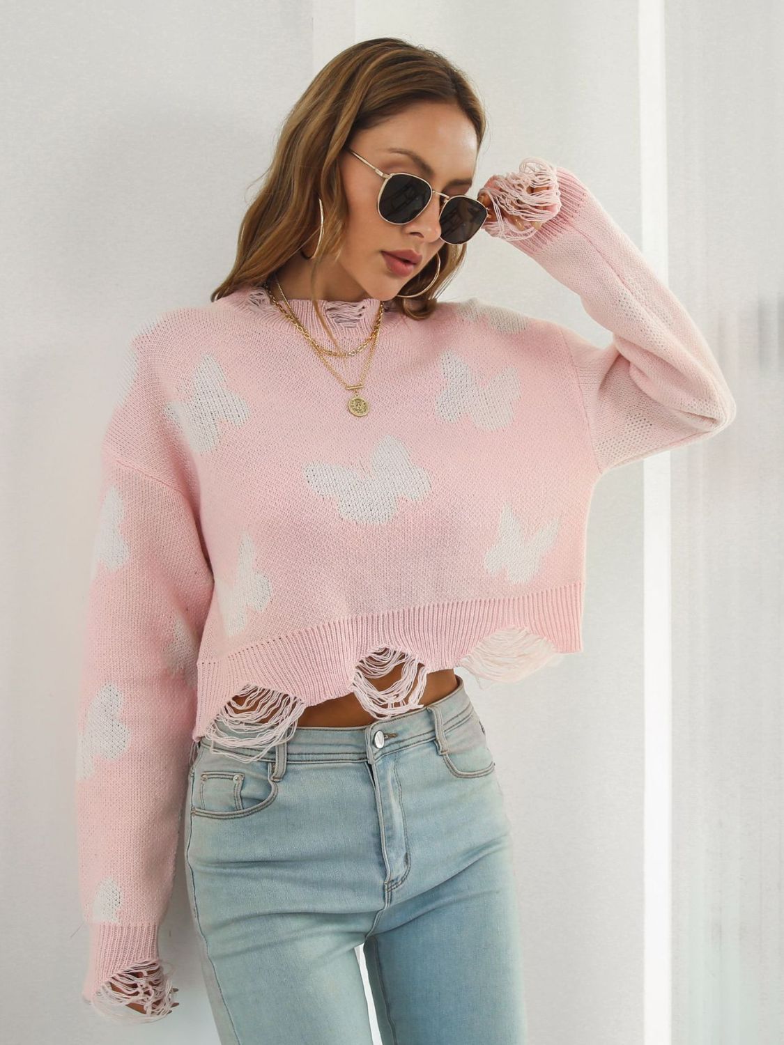 Distressed blush pink knit cropped sweater with white butterfly print and frayed hem.