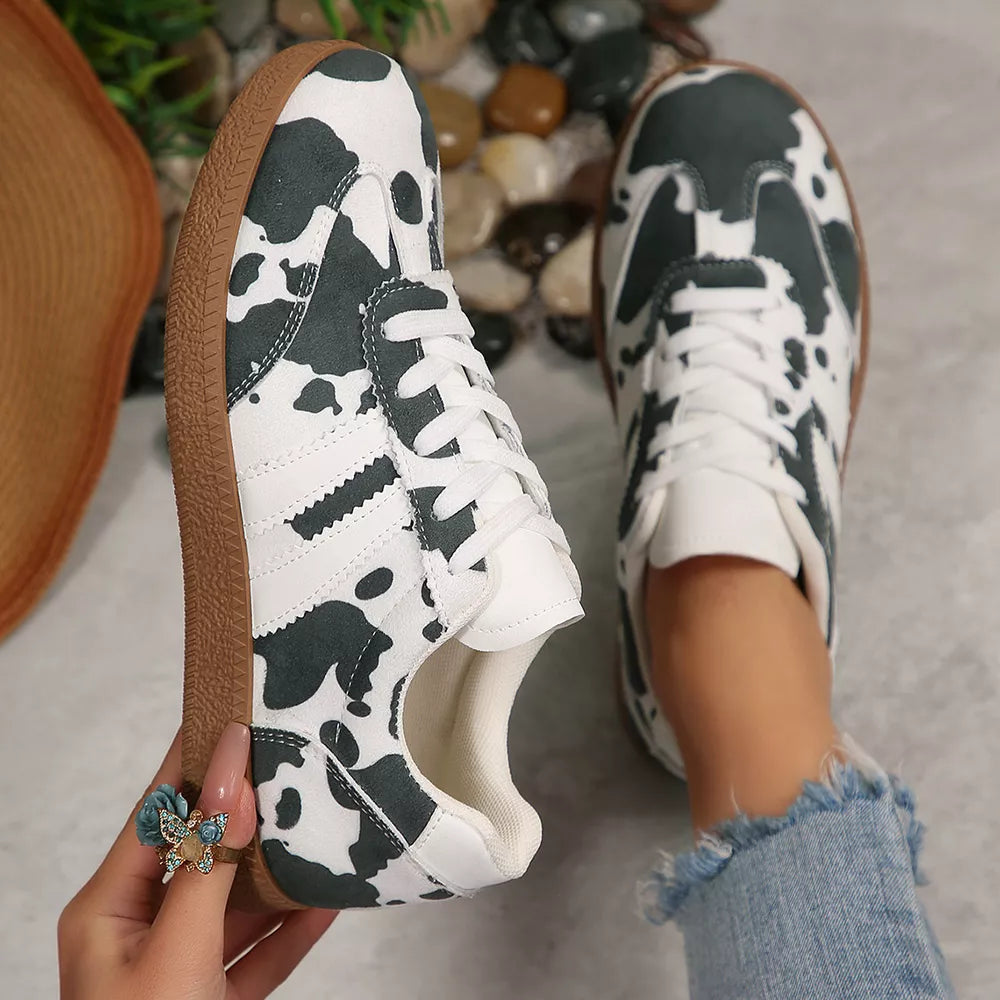 Trendy cow print low-top sneakers with white laces and brown soles.