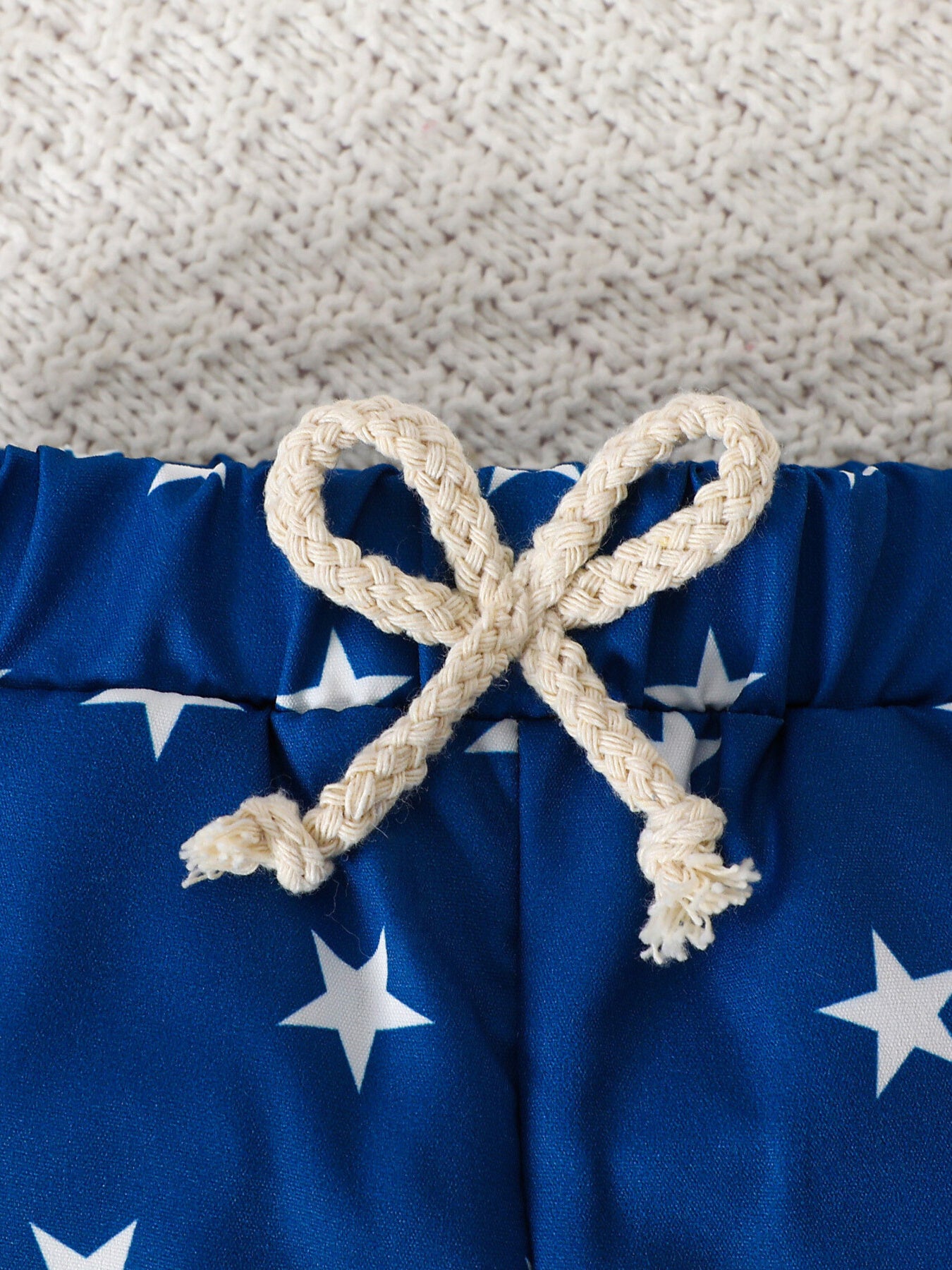 Blue cotton baby shorts with white stars and a cream rope drawstring.