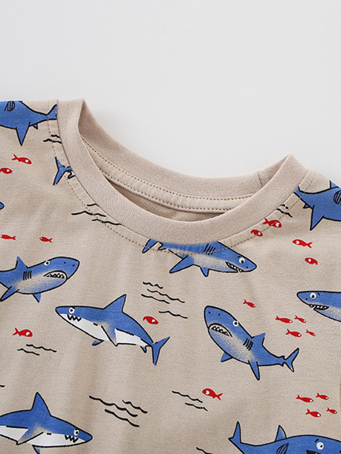 Toddler crew neck t-shirt with allover blue shark and red fish print on beige fabric.