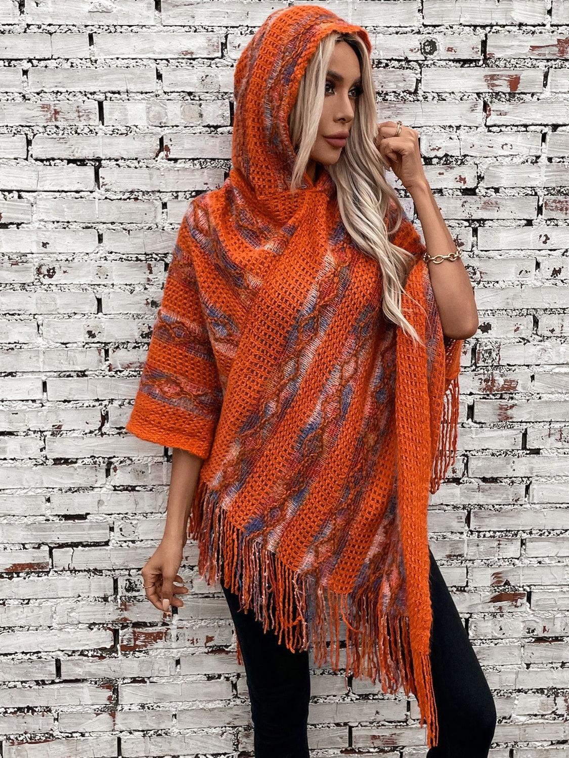 Terracotta hooded fringed knit cape with open weave and colorful accents.