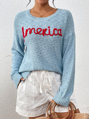 Pastel blue knit sweater with red embroidered "America" text, crew neck, long sleeves.