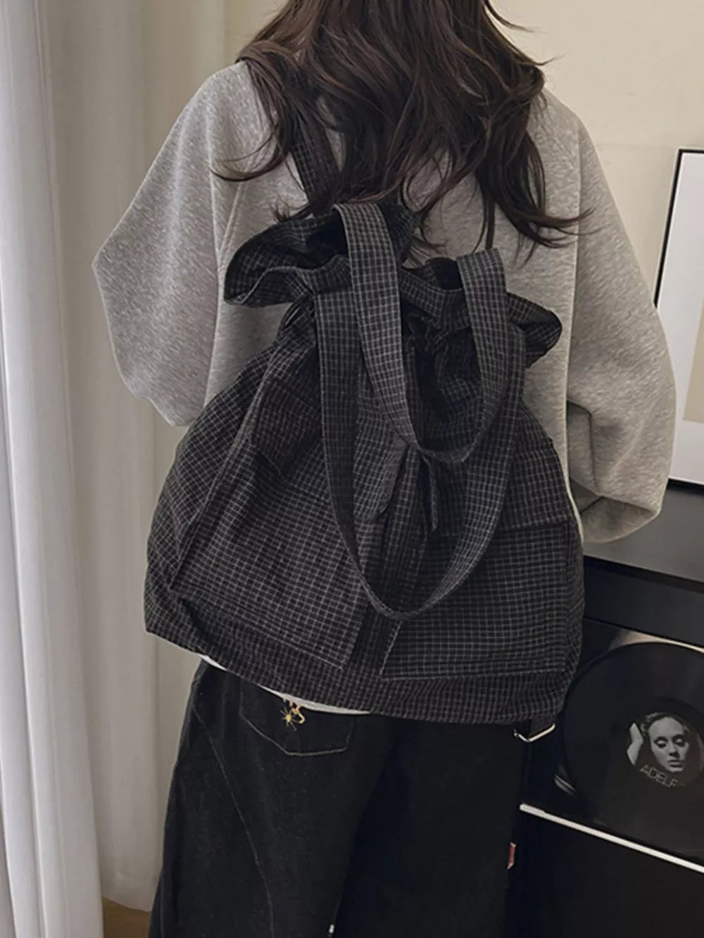 Grey plaid drawstring backpack with two front pockets and adjustable straps.