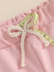 Pink cotton baby outfit detail with drawstring and measuring tape