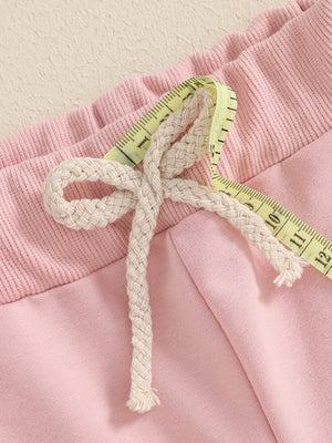 Pink cotton baby outfit detail with drawstring and measuring tape