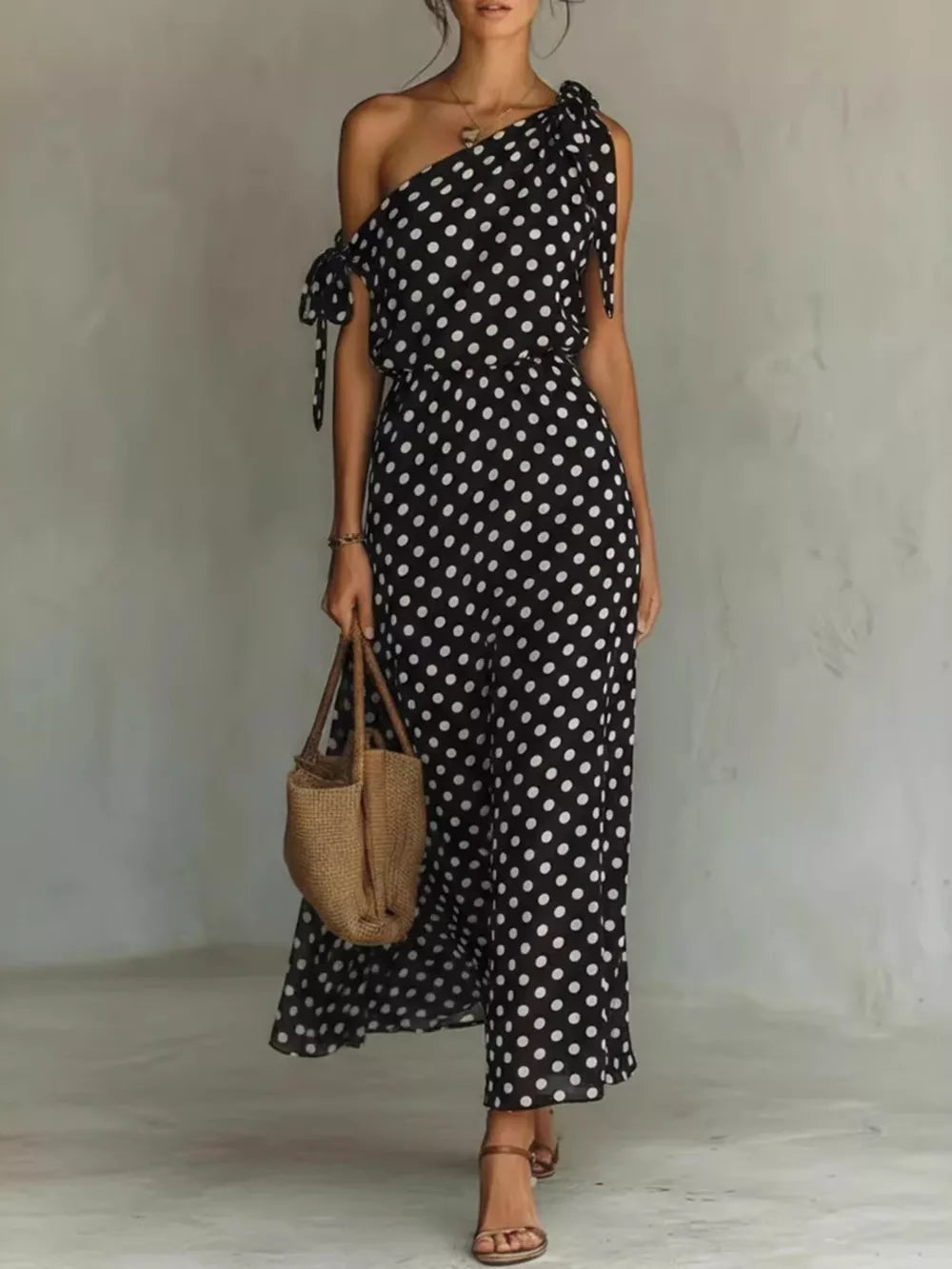 Black polka dot one-shoulder maxi dress with tie details and a flowing skirt.