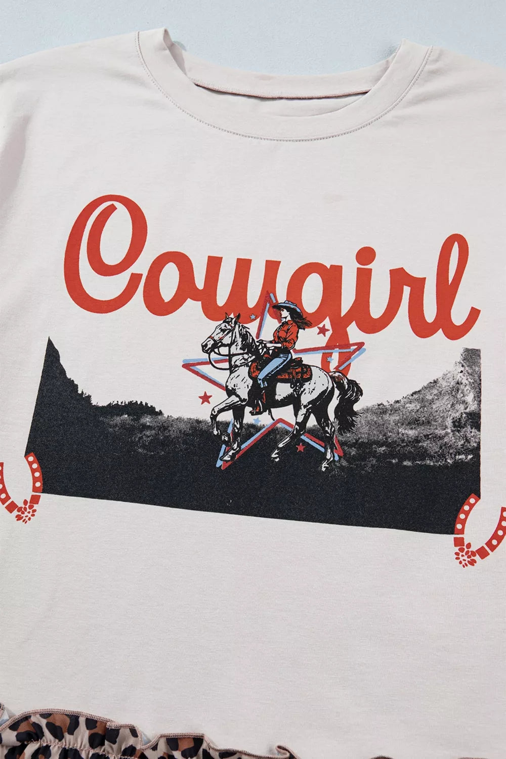 Cowgirl graphic tee in cream cotton blend with ruffled leopard hem.