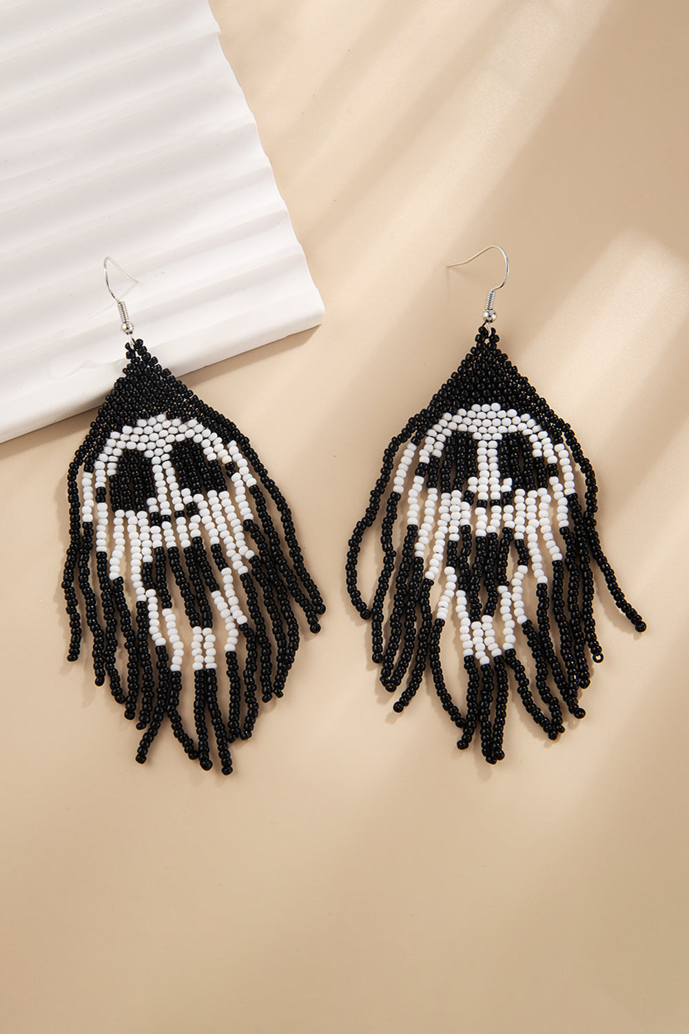 Beaded skull fringe earrings in black and white with dangling strands.