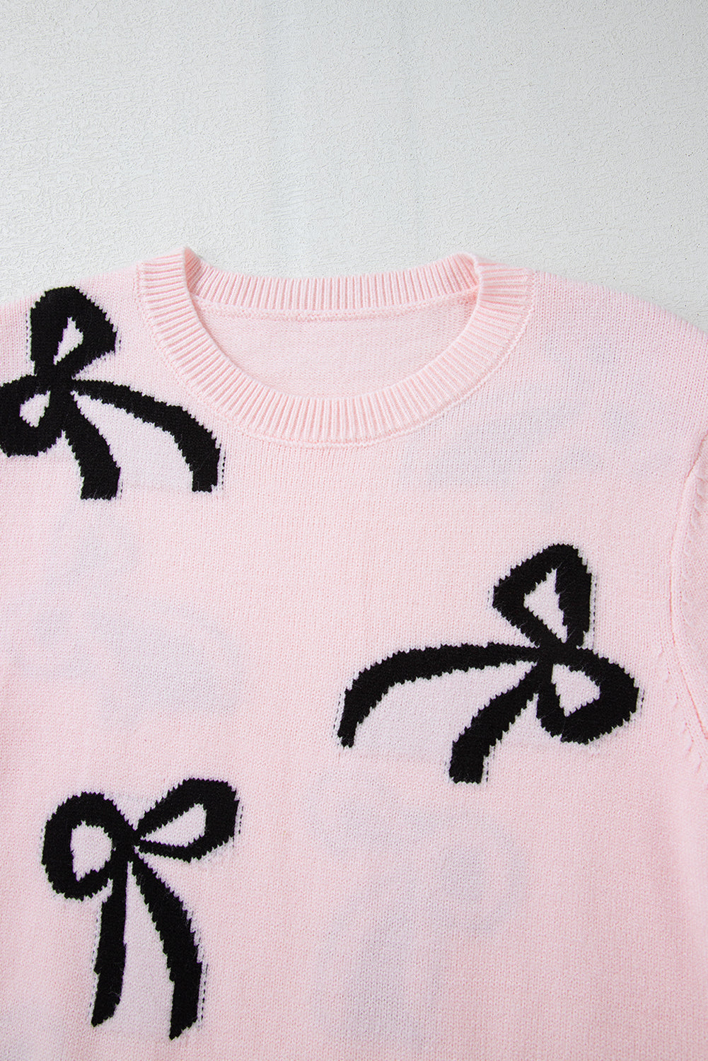 Pink knit crewneck sweater with black bow motifs and ribbed neckline.