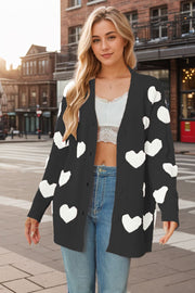Black acrylic knit cardigan with white heart appliques, button front, and long sleeves.