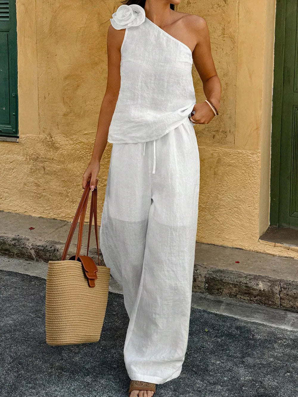 White cotton one-shoulder top with floral embellishment and wide-leg pants.