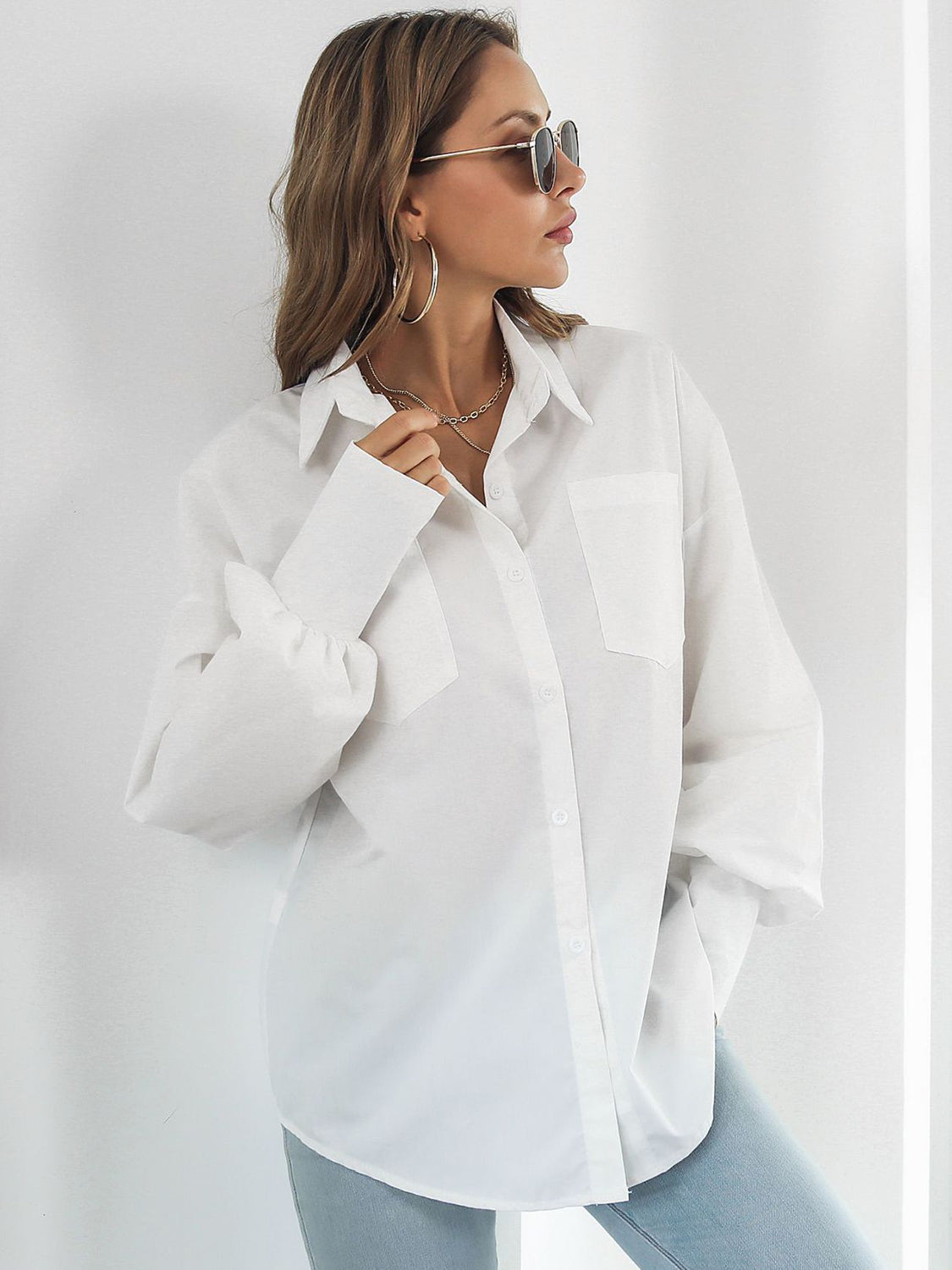 White oversized poplin blouse with blouson sleeves and button front, styled with jeans.