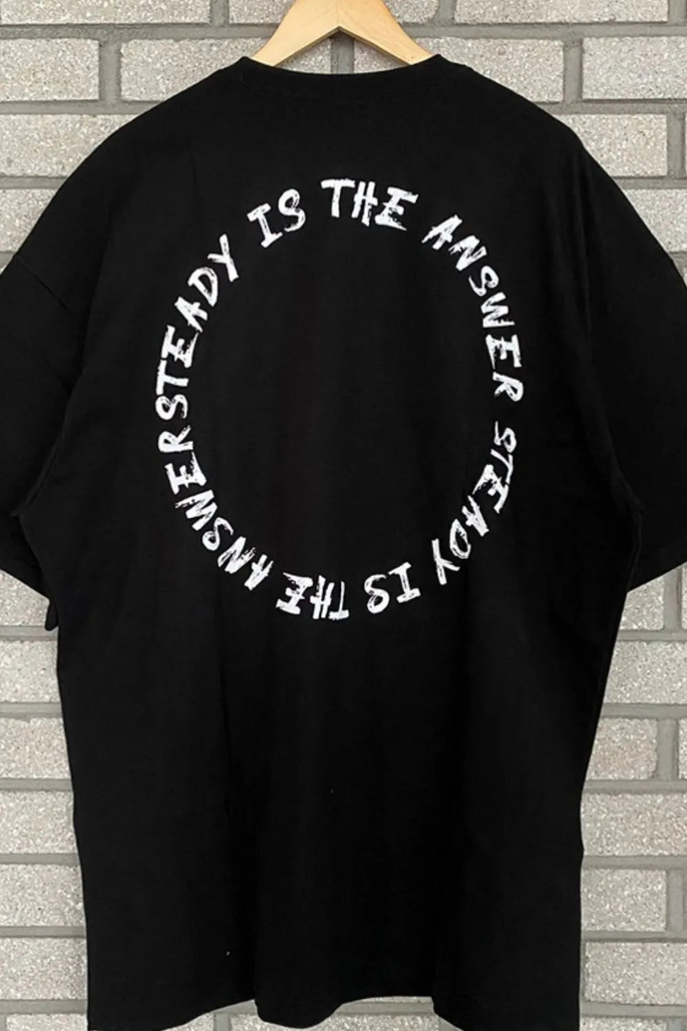 Black oversized t-shirt with white circle text graphic saying "UNSTEADY IS THE ANSWER STEADY IS THE ANSWER