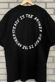 Black oversized t-shirt with white circle text graphic saying "UNSTEADY IS THE ANSWER STEADY IS THE ANSWER