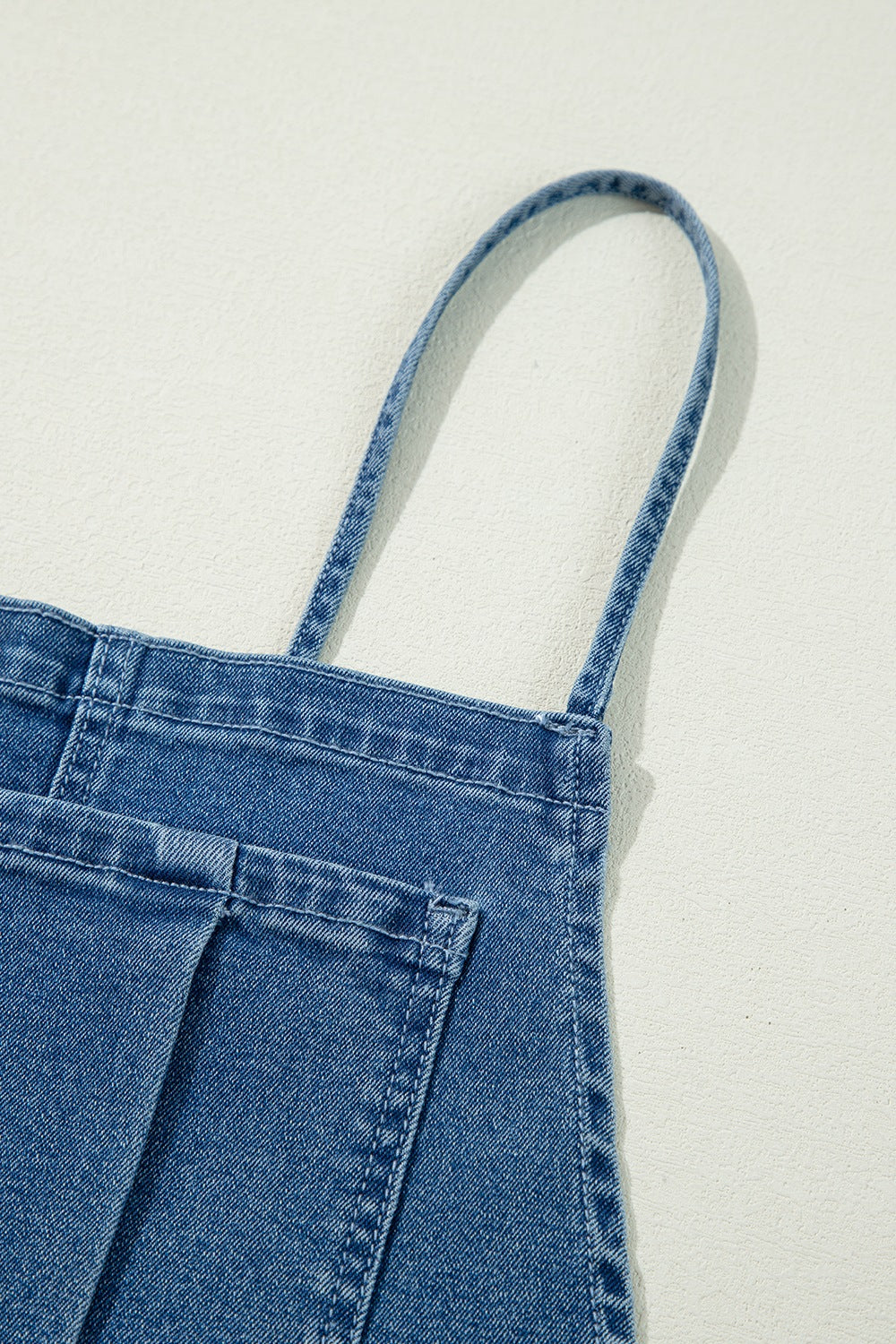 Denim wide-leg overalls in medium wash with adjustable straps and buttoned details.
