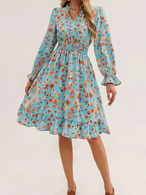 Pastel blue floral dress with smocked waist, ruffled hem, and long sleeves.