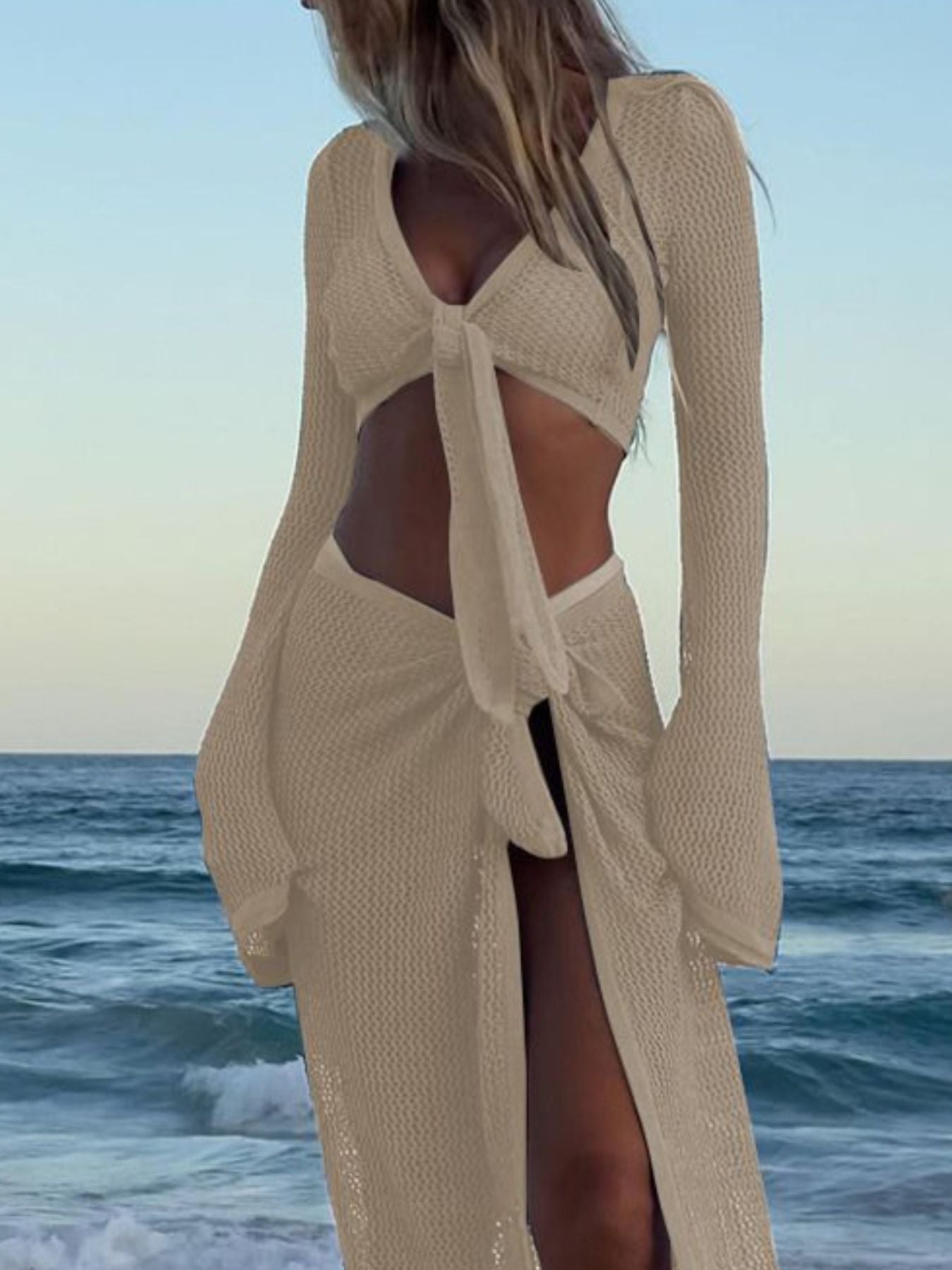 Beige openwork knit two-piece sweater set with tie-front cropped top and high-slit skirt.