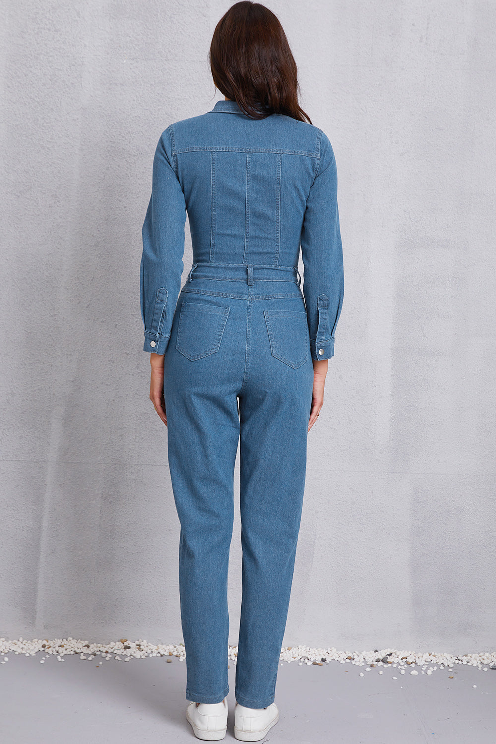 Denim utility jumpsuit in medium wash with defined waist and button cuffs.